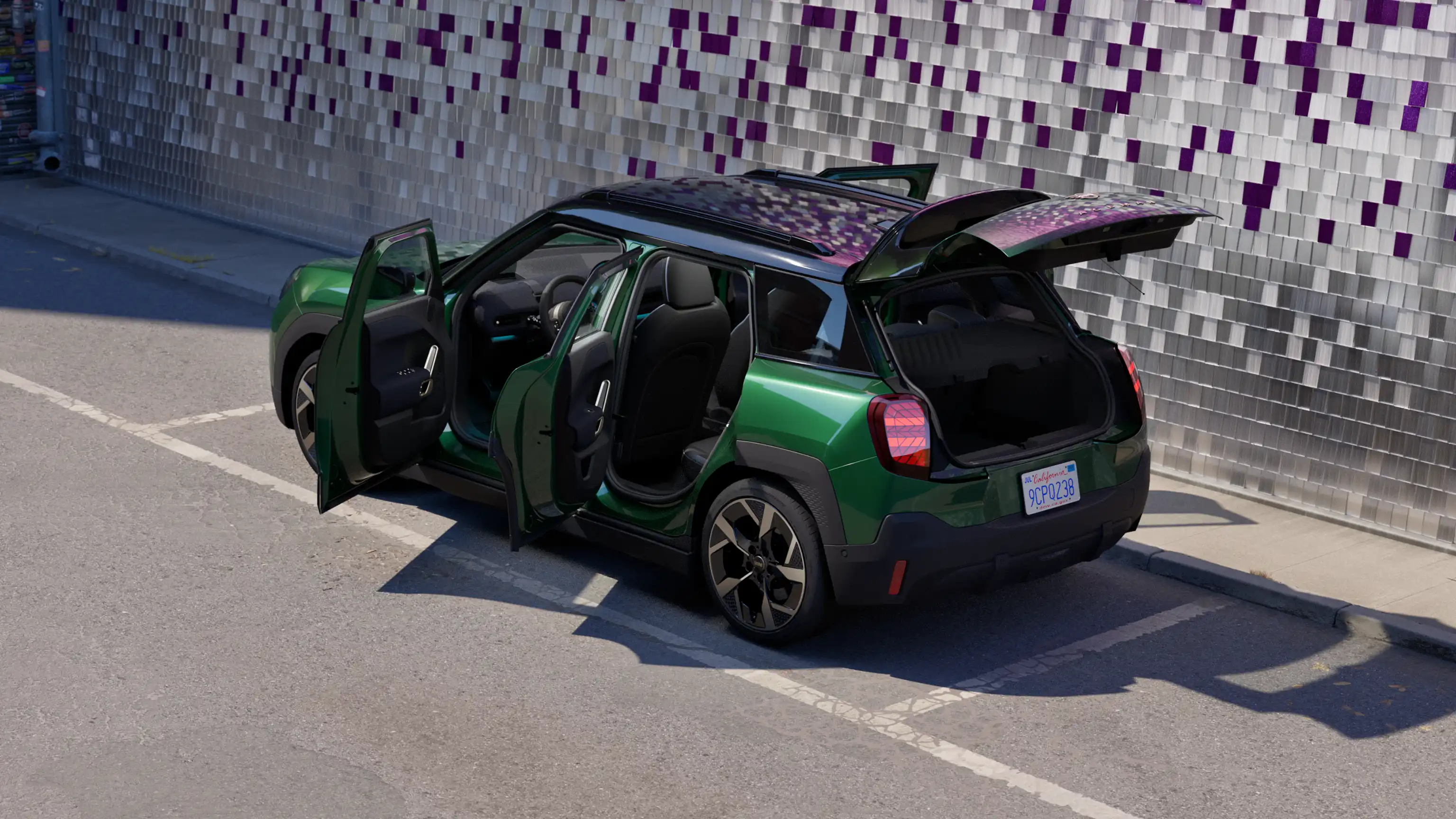 Zadný pohľad na zaparkované čisto elektrické MINI Aceman vo farbe British Racing Green na parkovisku s otvorenými dverami a farebnou stenou v pozadí
