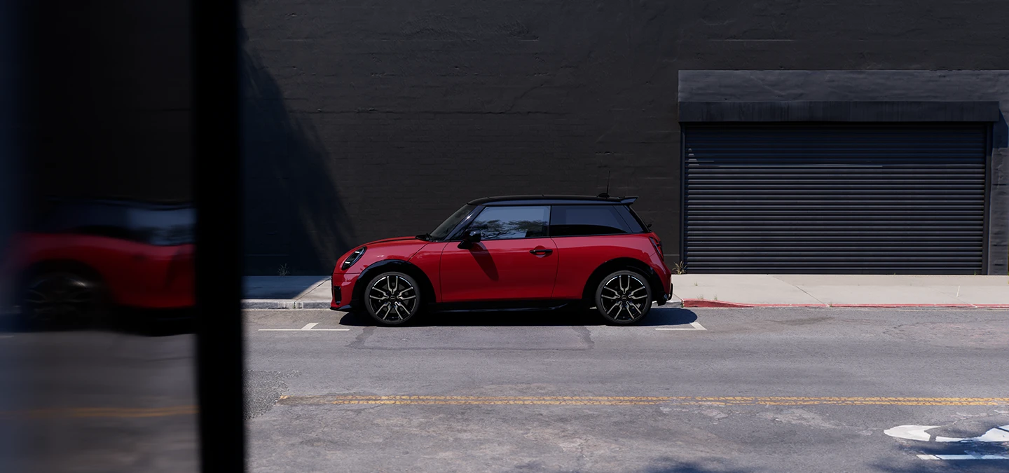 Bočný pohľad na MINI Cooper vo farbe Chili Red so strechou Black na parkovisku.
