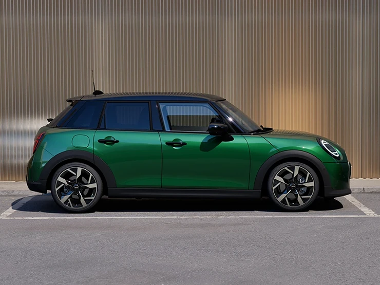 Bočný pohľad na MINI Cooper 5-dverové vo farbe v British Racing Green so strechou Black na parkovisku.