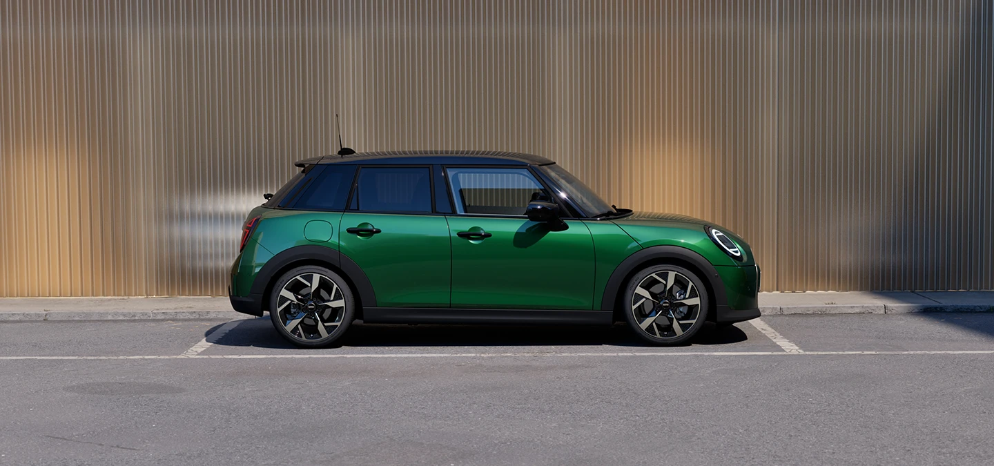 Bočný pohľad na MINI Cooper 5-dverové vo farbe v British Racing Green so strechou Black na parkovisku.