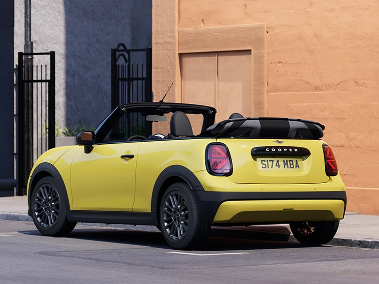 Zadný ľavý pohľad na MINI Cooper Cabrio vo farbe Sunnyside Yellow na parkovisku.