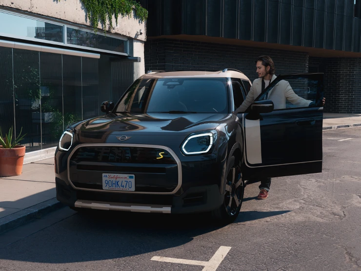 Pohľad spredu na čisto elektrické MINI Countryman vo farbe Midnight Black so strechou Vibrant Silver, na ulici.