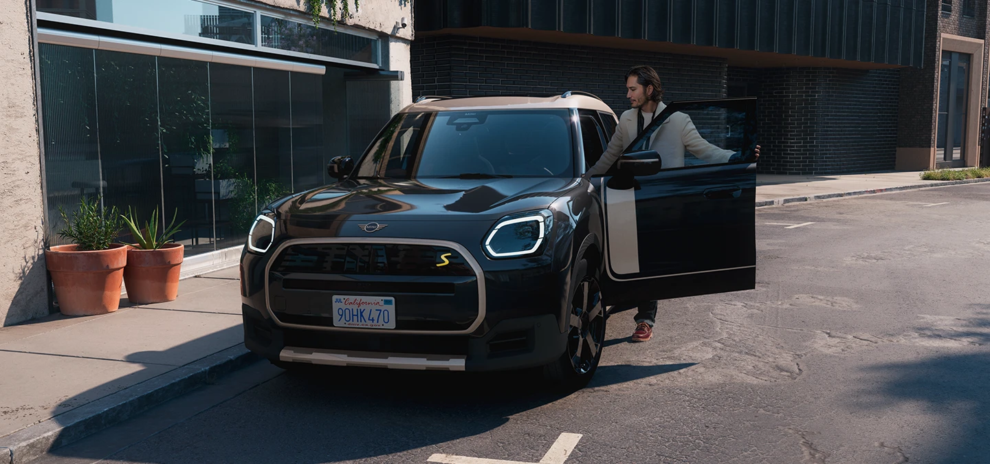 Pohľad spredu na čisto elektrické MINI Countryman vo farbe Midnight Black so strechou Vibrant Silver, na ulici.