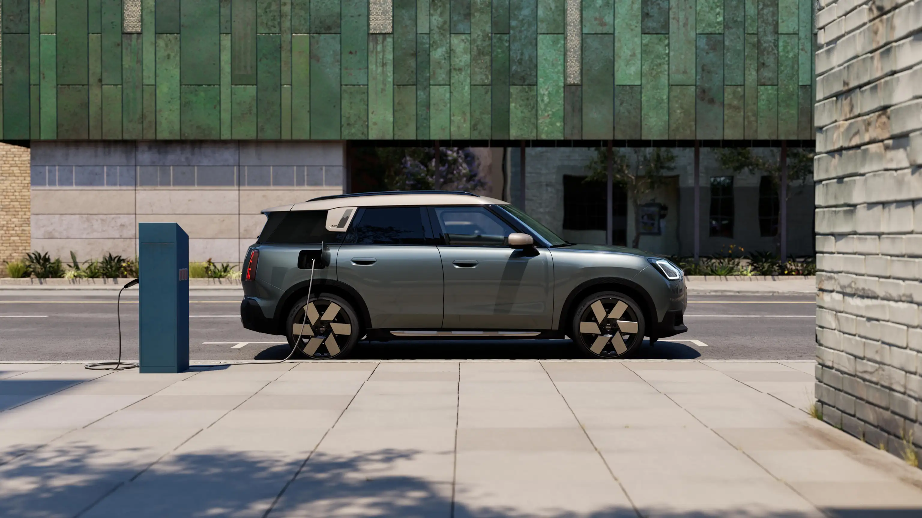 Pohľad na čisto elektrické MINI Countryman vo farbe Smokey Green so strechou Vibrant Silver na ulici