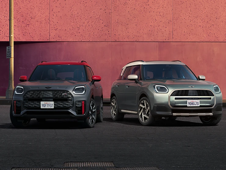 Pohľad spredu na MINI Countryman JCW vo farbe Legend Grey so strechou Red a MINI Countryman vo farbe Smokey Green so strechou Vibrant Silver, stojace vedľa seba.