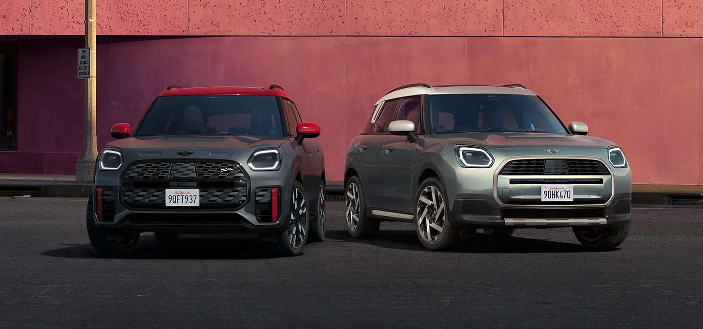 Pohľad spredu na MINI Countryman JCW vo farbe Legend Grey so strechou Red a MINI Countryman vo farbe Smokey Green so strechou Vibrant Silver, stojace vedľa seba.