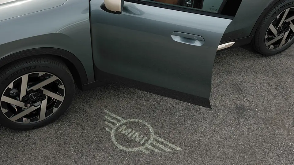 Pohľad na exteriér MINI Countryman s otvorenými dverami a uvítacím svetlom s logom MINI na zemi