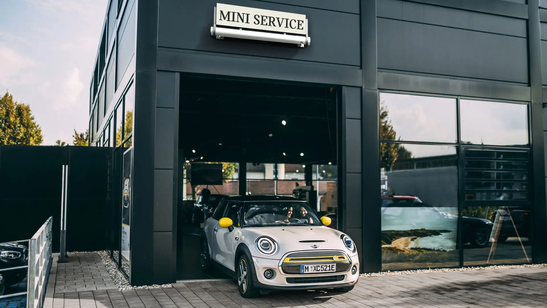 MINI servisný partner v priestoroch so zákazníčkou, ktorá vychádza so svojím novým MINI Electric do priestoru pred budovou