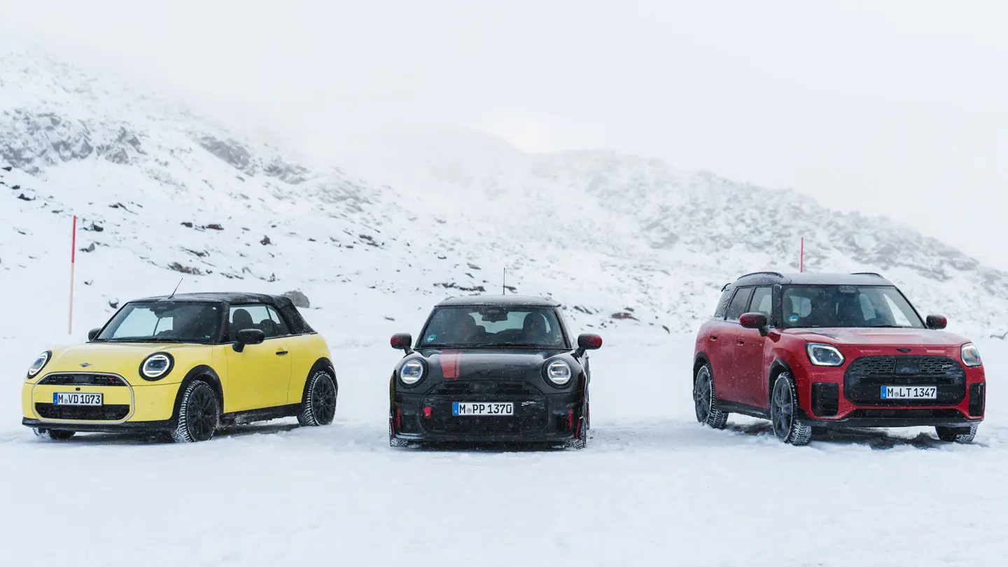 MINI Cooper Cabrio vo farbe Sunny Side Yellow, MINI John Cooper Works vo farbe Midnight Black II a MINI Countryman Cooper vo farbe Chili Red – stojace na zasneženej horskej ceste, pohľad spredu.