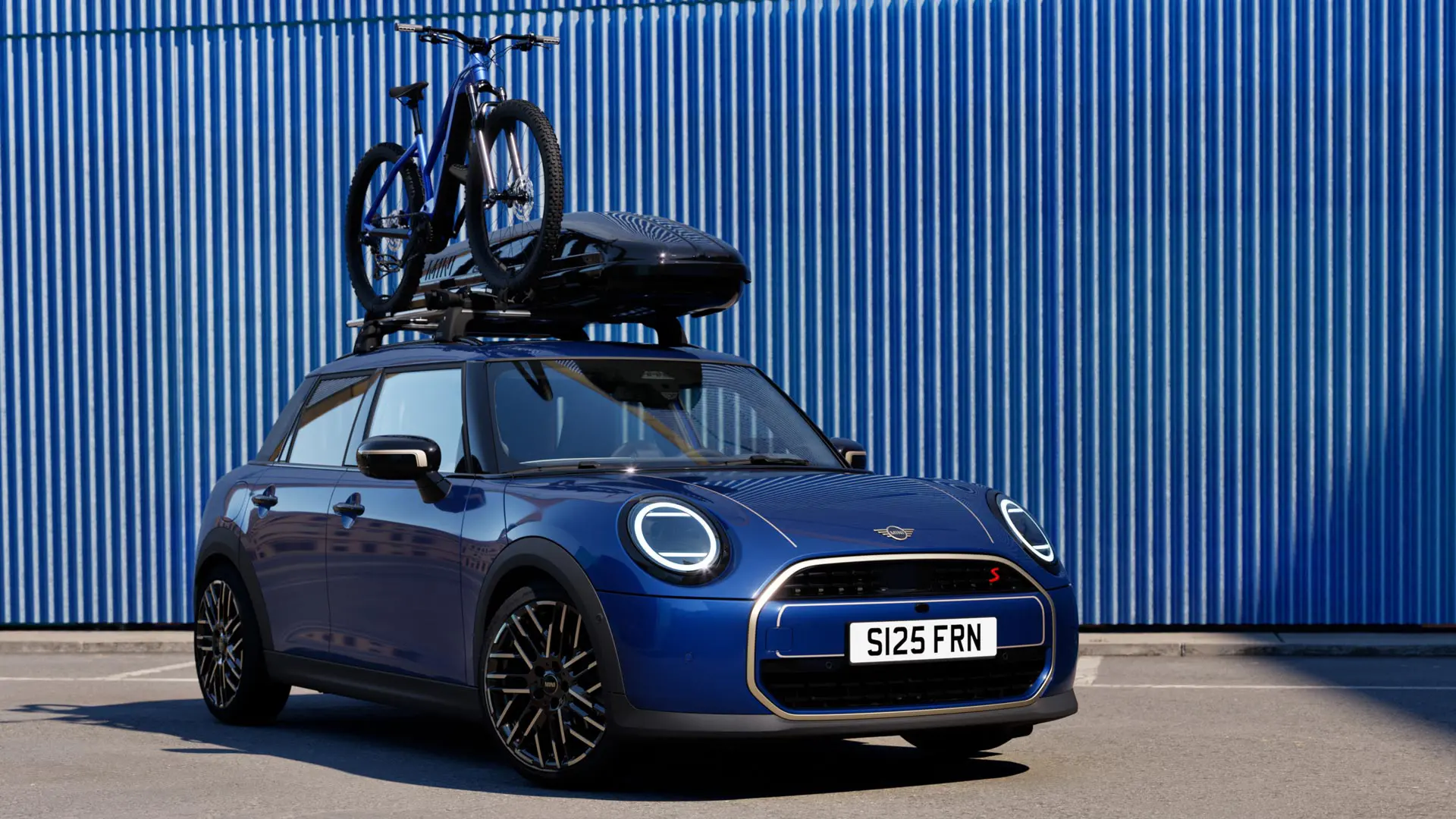 Pohľad spredu na MINI Aceman vo farbe Indigo Sunset Blue s MINI strešným nosičom bicyklov, na ktorom je horský bicykel a MINI strešný box 320.