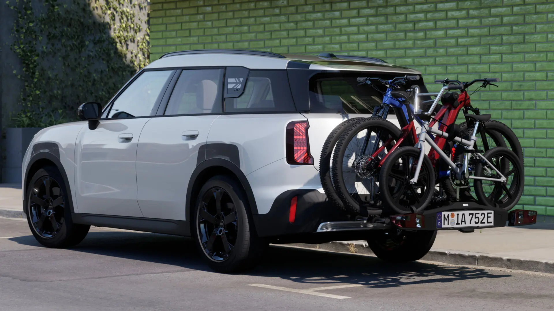 MINI Aceman vo farbe Nanuq White vybavené MINI zadným nosičom bicyklov Pro 3.0, na ktorom sú naložené dva horské bicykle a detský bicykel.