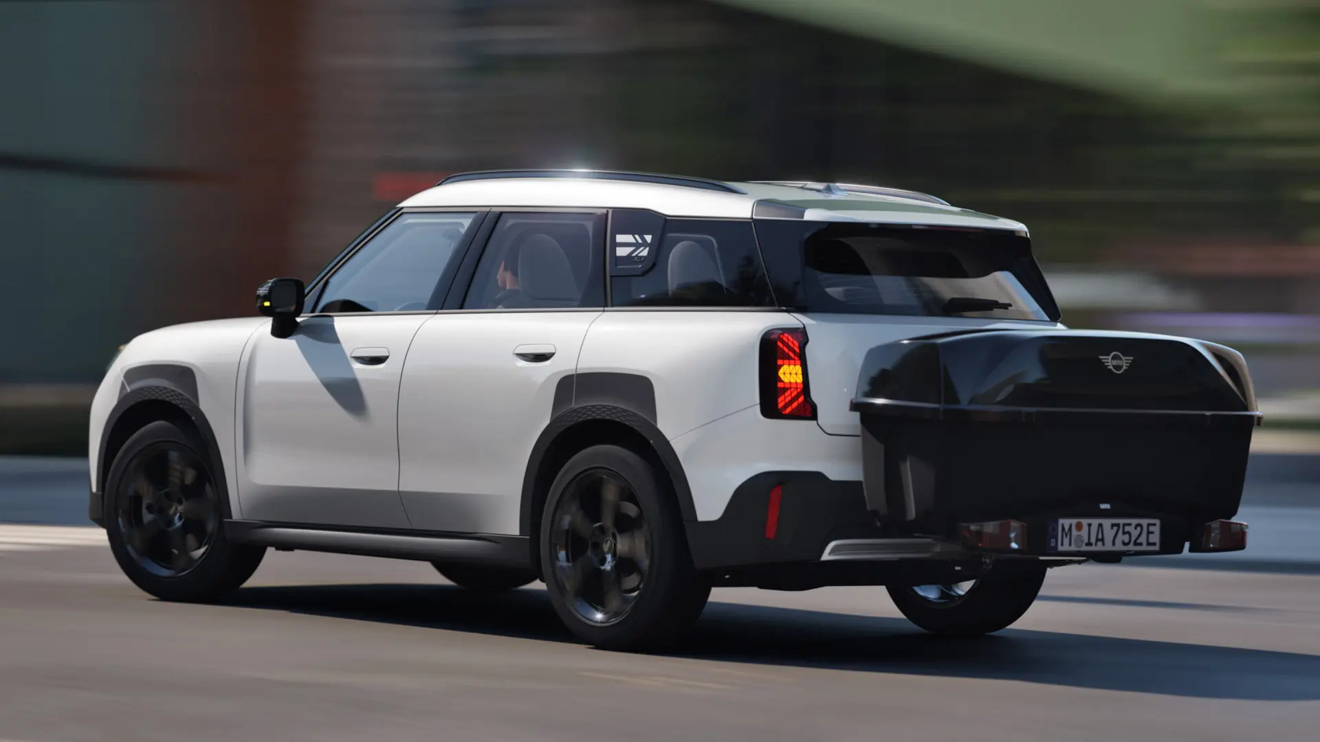 Zadný pohľad zboku na MINI Aceman vo farbe Nanuq White, vybavené MINI zadným nosičom bicyklov, na ktorom je MINI zadný box. 