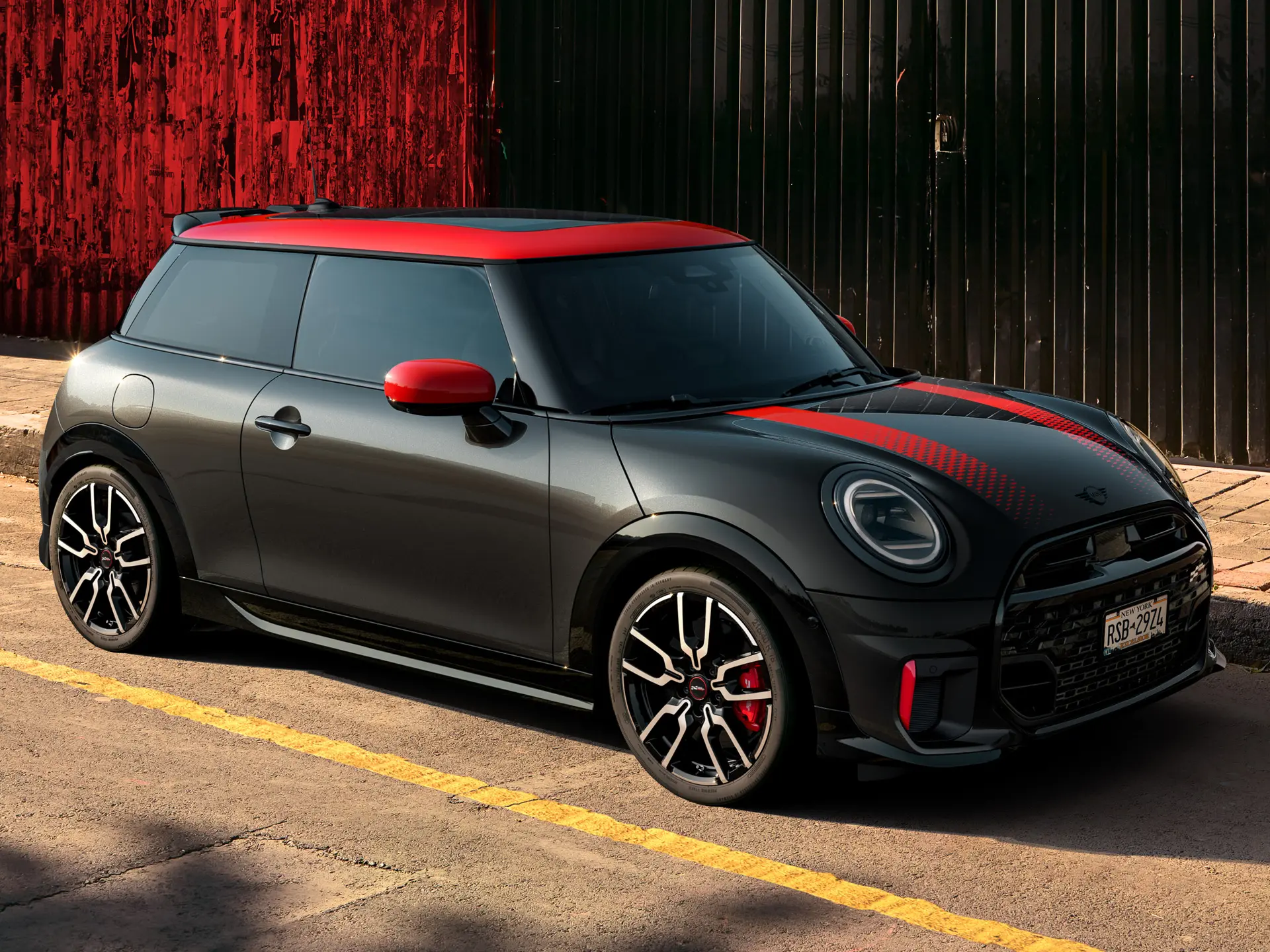 MINI John Cooper Works 3-dverové vo farbe Midnight Black so strechou a krytmi zrkadiel vo farbe Chili Red a červenými športovými pruhmi, zaparkované na ulici.