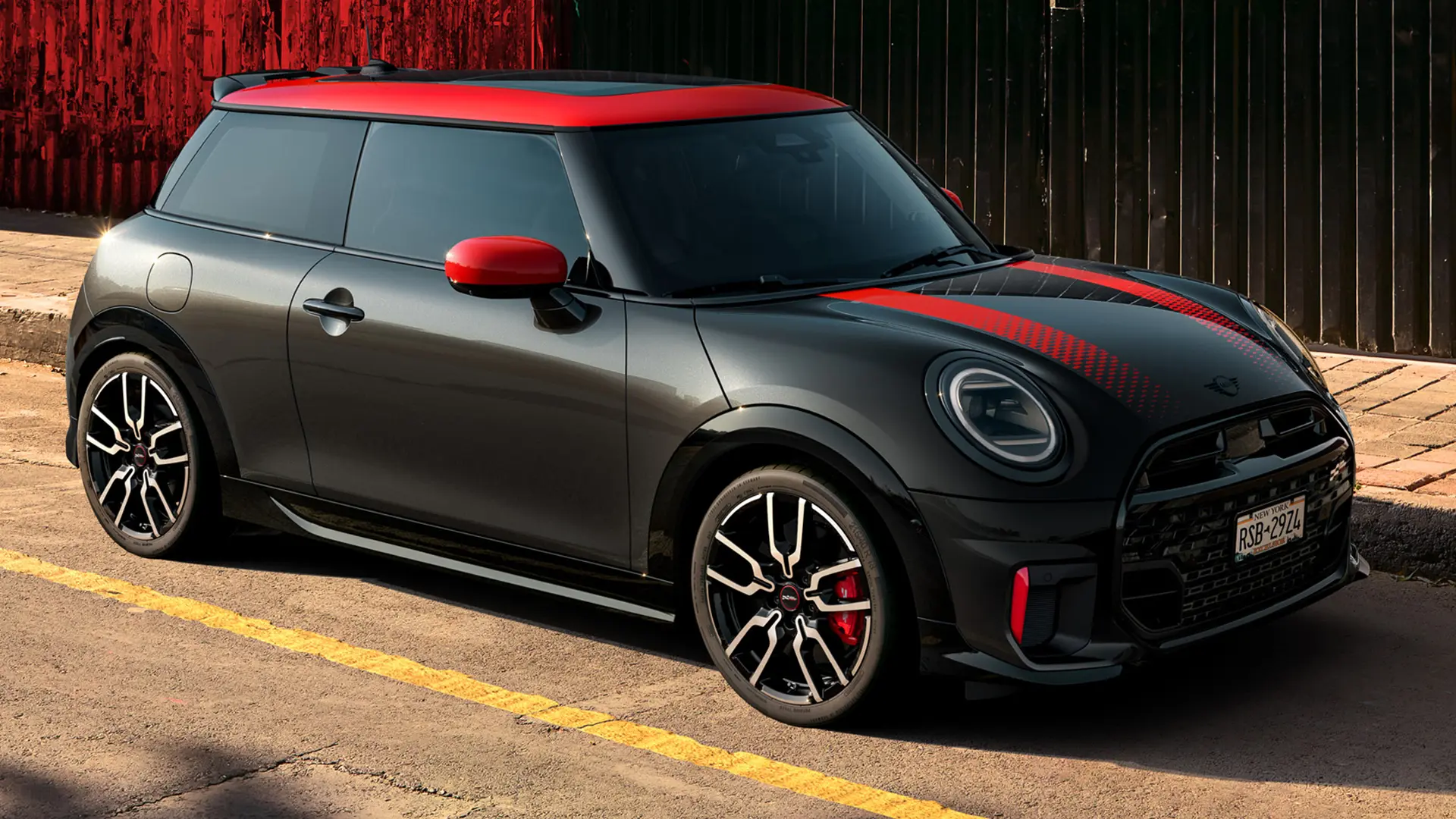 MINI John Cooper Works 3-dverové vo farbe Midnight Black so strechou a krytmi zrkadiel vo farbe Chili Red a červenými športovými pruhmi, zaparkované na ulici.