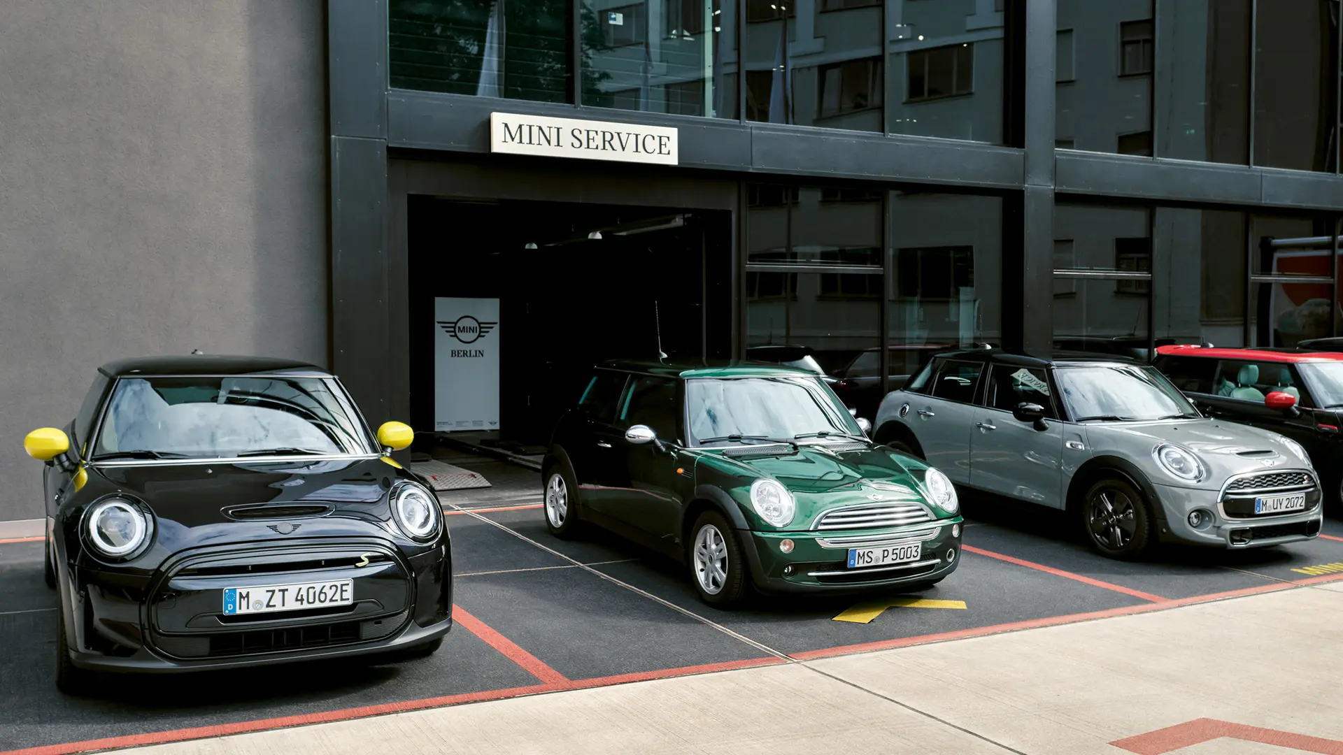 MINI Cooper Electric S v čiernej farbe pred MINI centrom, spolu s MINI Cooper 3-dverovým v zelenej farbe, MINI 5-dverovým v striebornej farbe a MINI JCW v čiernej farbe, predný pohľad. 