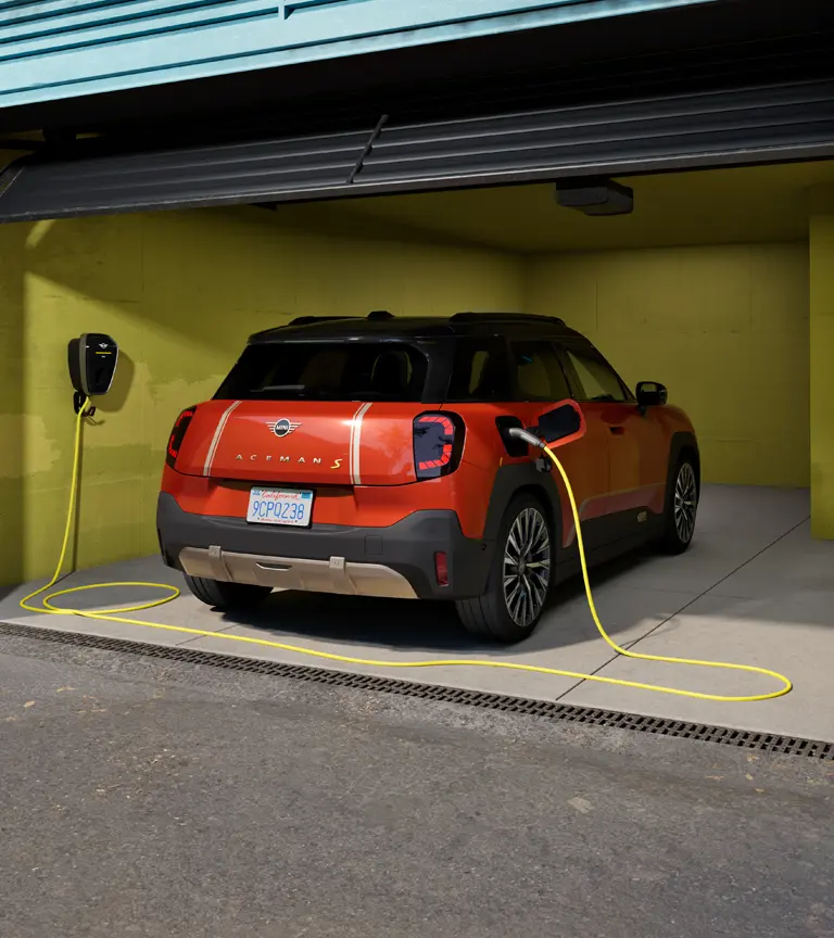 Čisto elektrické MINI Aceman S počas nabíjania zariadením MINI Wallbox Plus, zadný pohľad, v garáži.